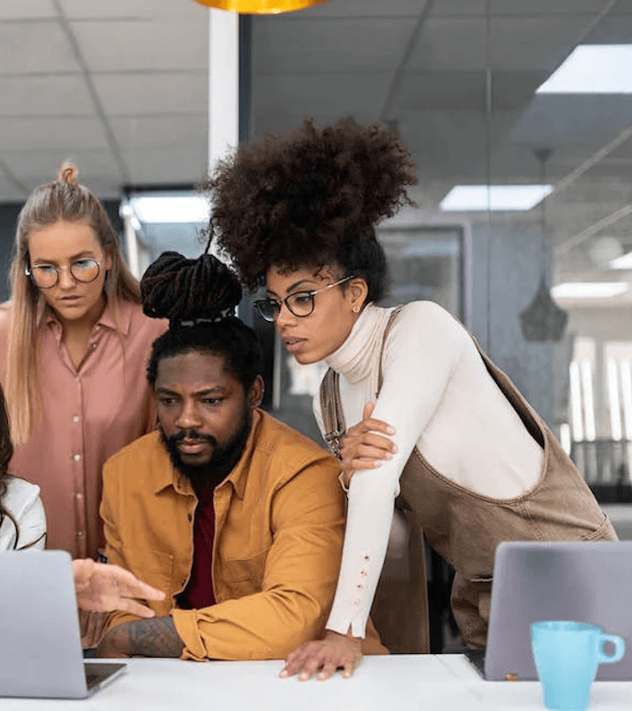 Three people are looking at a laptop in an office.